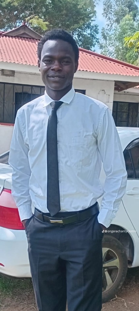 Ong'era Daniel, founder and Executive Director of Ong'era Brethren International Foundation, in a white shirt and tie, standing outside the foundation campus in Migori County, Kenya. TikTok: @ongeracharitycentre